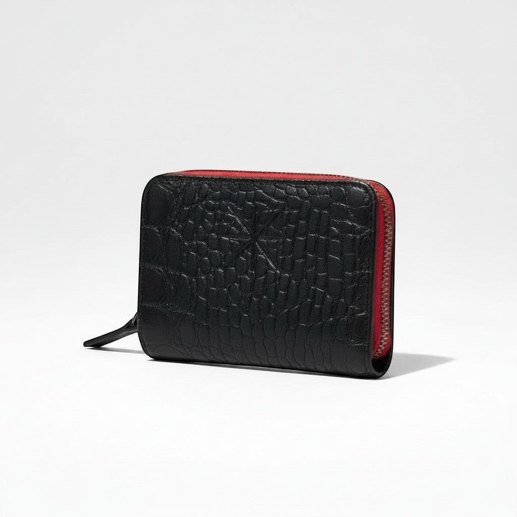 Portefeuille zippé La Stella en cuir noir texturé croco avec doublure rouge. Format compact pour cartes et billets.